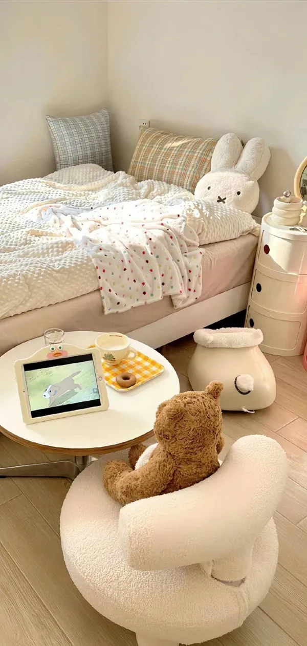 Một phòng ngủ nhỏ có giường, gấu bông và bàn hình nền màu nâu nhạt
