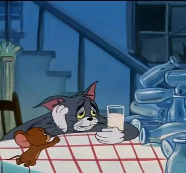 Một con mèo hoạt hình đang ngồi ở bàn meme buồn