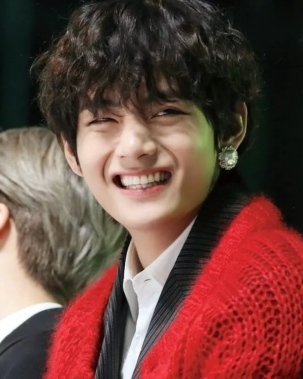 Ảnh bts có một chàng trai trẻ đang mỉm cười và mặc chiếc áo len màu đỏ