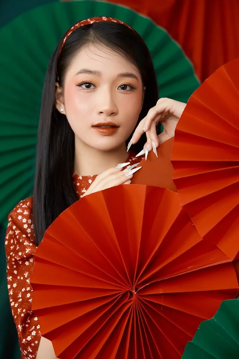 Dáng chụp ảnh tết đây là một người phụ nữ đang cầm hâm mộ màu đỏ và xanh lá cây trước mặt