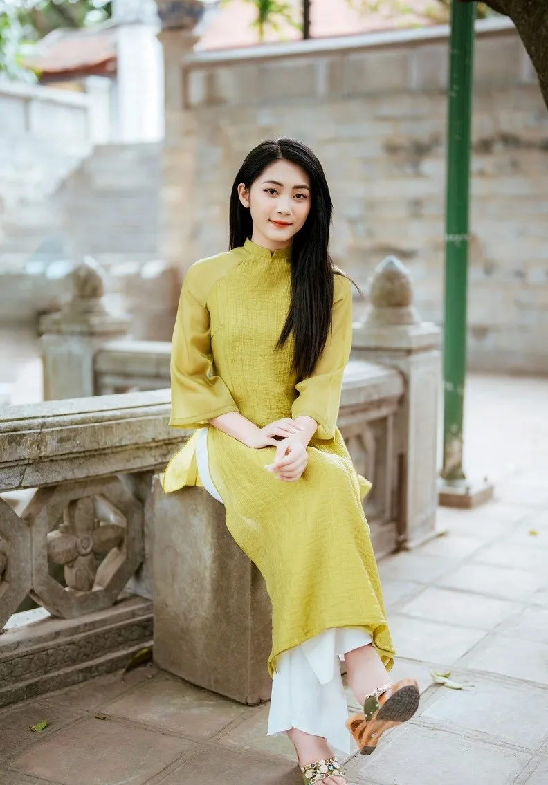 Phông chụp ảnh tết có một người phụ nữ ngồi trên ghế đá trong chiếc váy màu vàng
