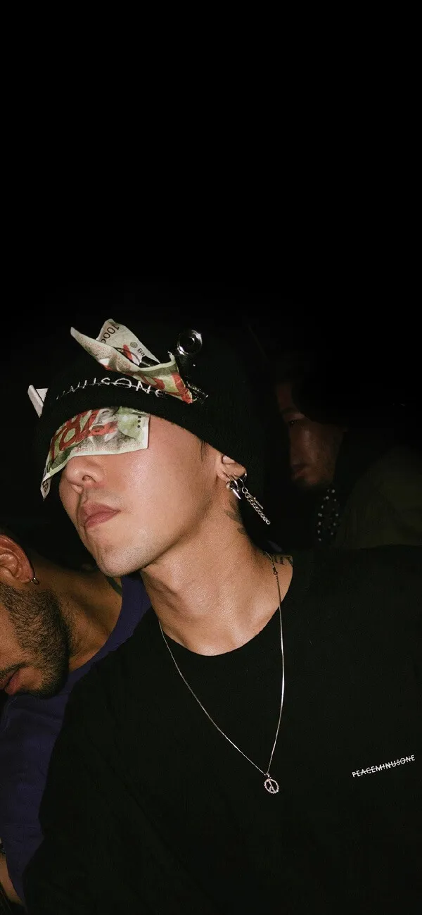 Ảnh của g-dragon người đàn ông tóc vàng mặc áo đen và mũ bandana ngồi cạnh một khác