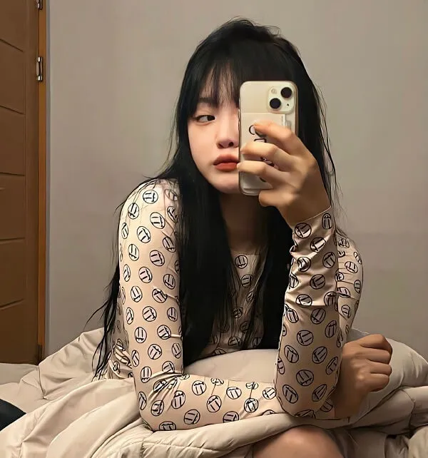 Có một người phụ nữ ngồi trên giường chụp ảnh tự sướng với điện thoại di động