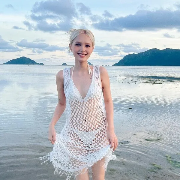 Ảnh gái xinh việt nam người phụ nữ tóc vàng mặc váy crocheted trắng đứng trên bãi biển bên cạnh nước