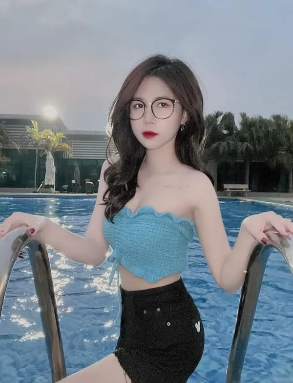 Ảnh gái xinh tóc dài đeo kính có một người phụ nữ trong chiếc áo màu xanh và quần short đen bên hồ bơi