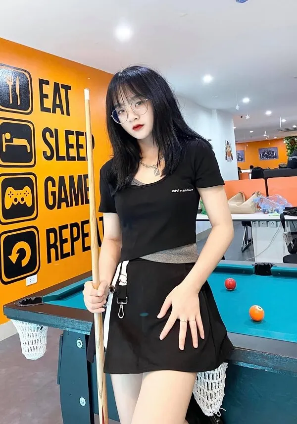Ảnh gấm kami sexy người phụ nữ mỉm cười trong chiếc váy đen đứng cạnh bàn bi -a với một thanh