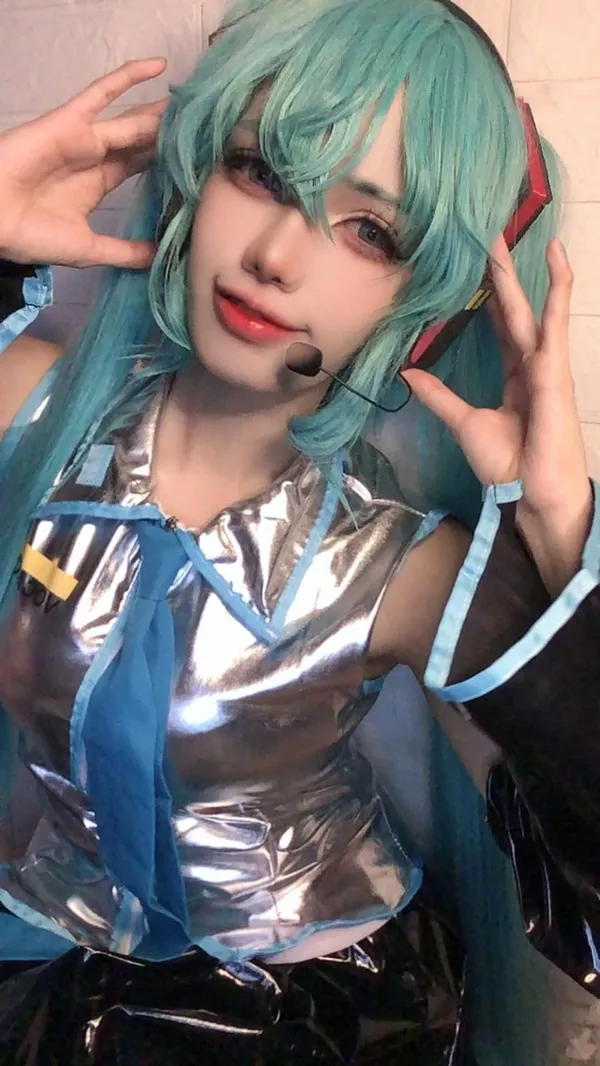 Ảnh hatsune miku hiếm người phụ nữ cười với mái tóc xanh và tai nghe mặc trang phục bạc sáng bóng