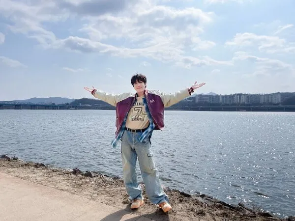 Ảnh dìm của j-hope có một người đàn ông đang đứng bên nước với hai cánh tay dang rộng