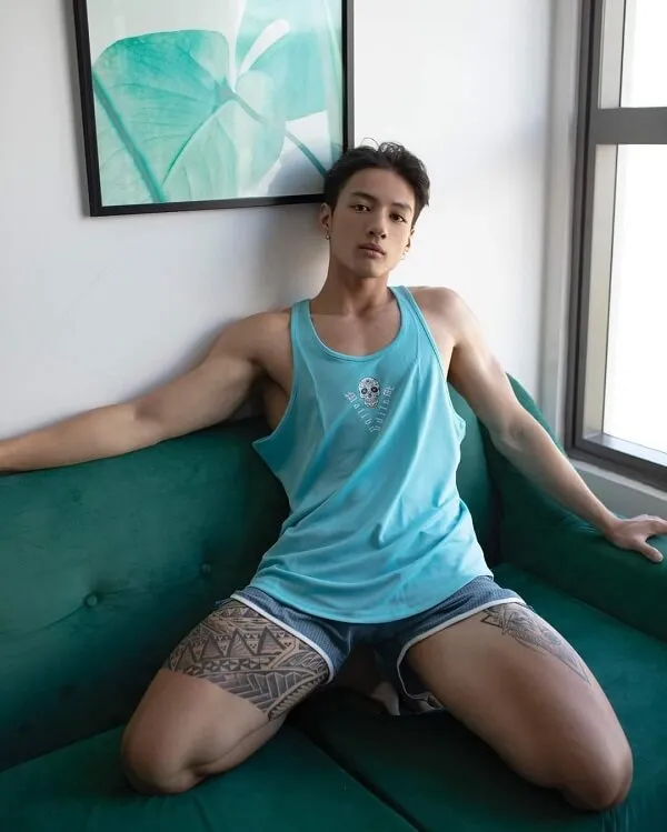 Hình ảnh hot boy đẹp trai ai đó đang ngồi trên một chiếc ghế dài màu xanh lá cây với xăm cánh tay của anh ấy