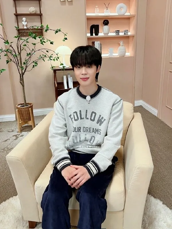 Ảnh jimin dễ thương cậu bé ngồi trên ghế trong phòng khách mặc áo len và quần jean