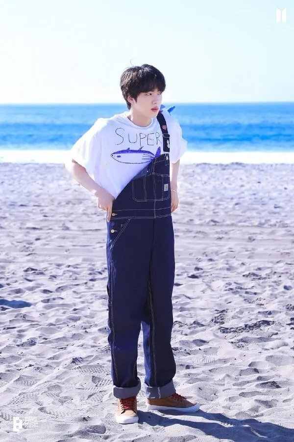 Ảnh jin bts có một chàng trai trẻ đứng trên bãi biển với hai tay hông