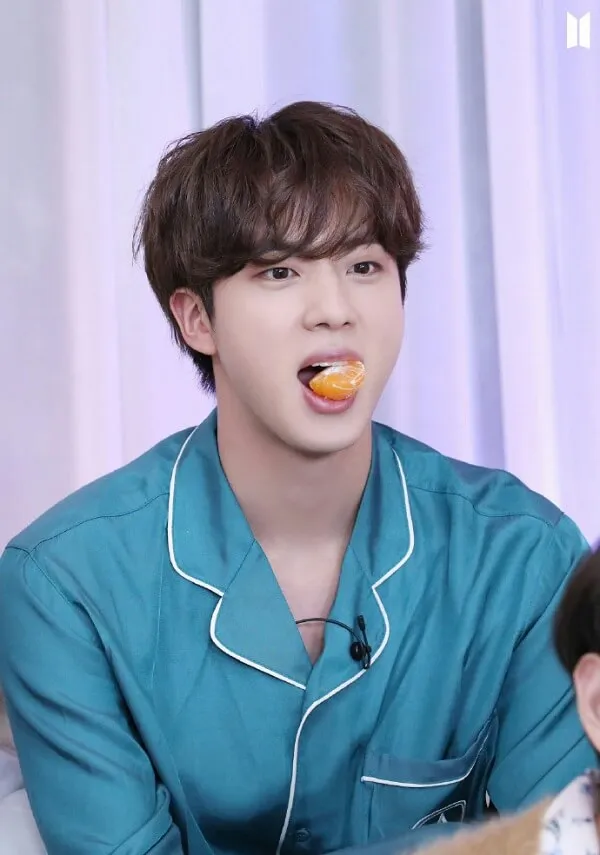 Hình ảnh jin bts người đàn ông châu mặc đồ ngủ màu xanh ăn một lát cam khi ngồi trên ghế dài