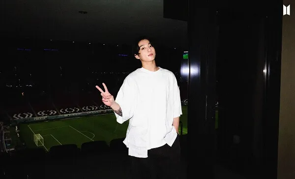Ảnh jungkook có một người đàn ông mặc áo sơ mi trắng và quần đen tạo dáng cho bức tranh