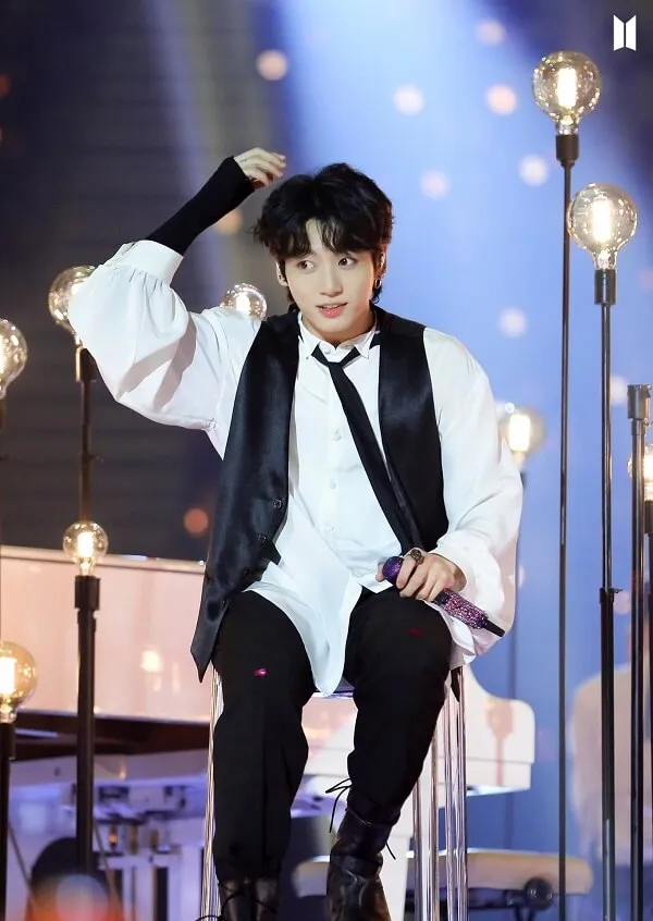 Ảnh jungkook ngầu có một người đàn ông mặc áo sơ mi trắng và vest đen ngồi trên ghế