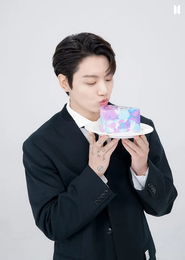 Ảnh jungkook người đàn ông châu trong bộ tuxedo ăn một miếng bánh với rắc lên đó
