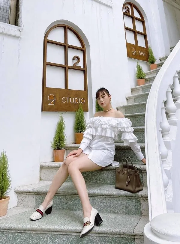 Diễn viên phương oanh người phụ nữ ngồi trên những bậc thang của một tòa nhà màu trắng với chiếc vali trước mặt