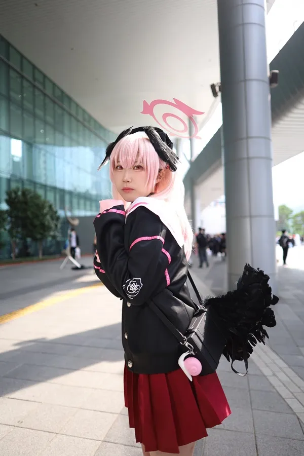 Shimoe koharu cosplay có một người phụ nữ mái tóc màu hồng mặc áo khoác đen và váy