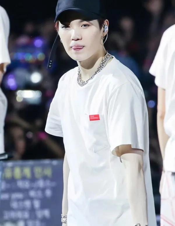 Ảnh suga cute người đàn ông mặc áo phông trắng và mũ đen đứng trước đám đông