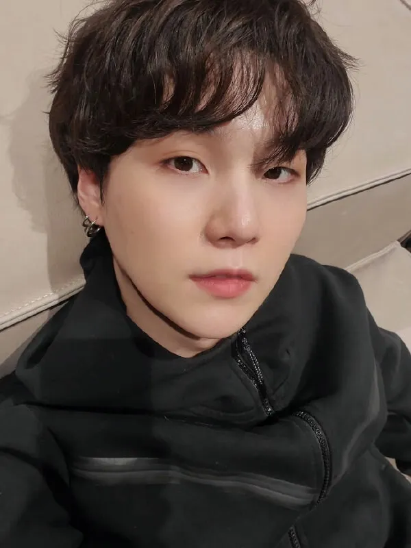 Ảnh suga mới nhất có một chàng trai trẻ với chiếc áo khoác màu đen ngồi trên ghế dài