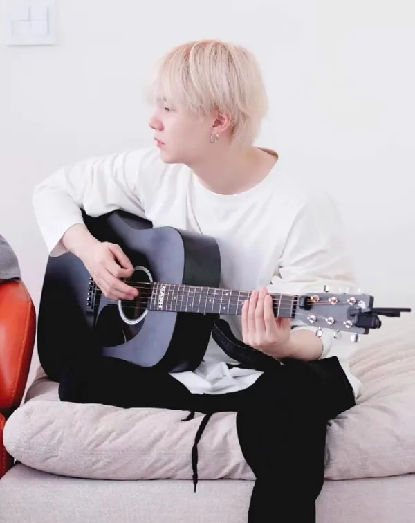 Ảnh suga mới nhất có một người đàn ông đang ngồi trên chiếc ghế dài với cây guitar