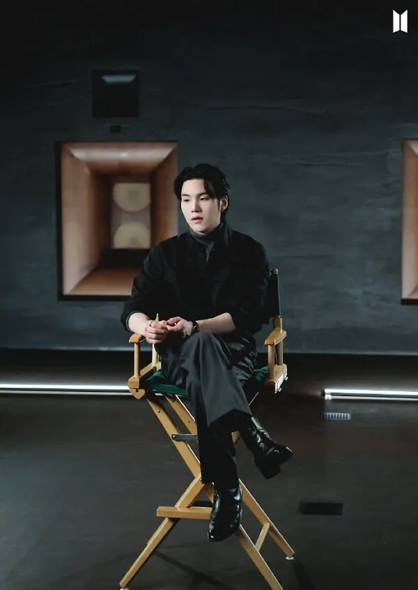Ảnh suga bts chân dung của một người đàn ông ngồi trên ghế giám đốc trong căn phòng tối