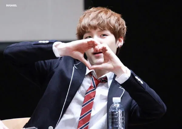 Ảnh suga bts có một chàng trai trẻ trong bộ đồ và cà vạt ngồi vào bàn