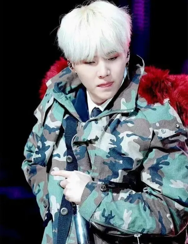 Ảnh suga bts có một người đàn ông mặc áo khoác ngụy trang cầm micro