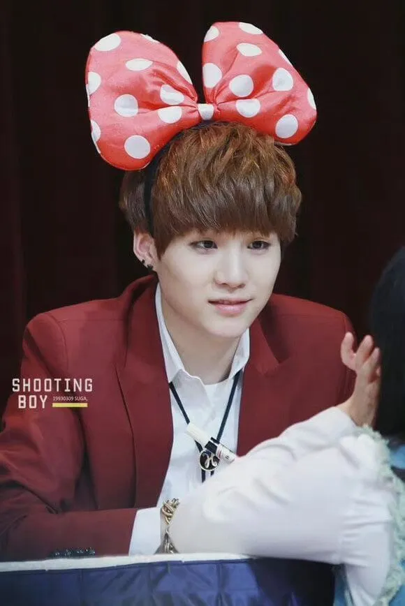 Ảnh suga mới nhất có một người đàn ông mặc bộ đồ màu đỏ với cây cung trên đầu