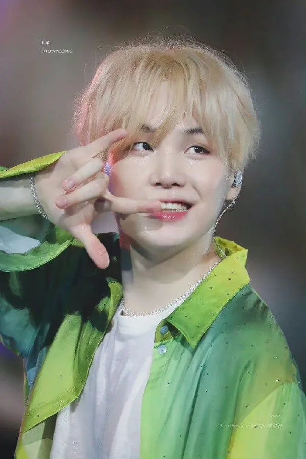Ảnh suga mới nhất cậu bé với mái tóc vàng và áo khoác màu xanh lá cây làm một dấu hiệu hòa bình