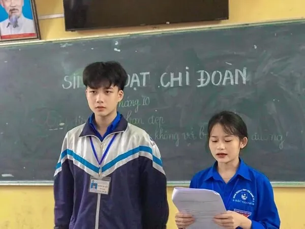 Ảnh trai đẹp lớp có hai người đứng trước bảng đen cầm giấy tờ
