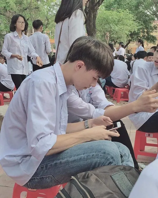 Ảnh trai đẹp học sinh họ đang ngồi trên những chiếc ghế màu đỏ nhìn vào điện thoại di động của