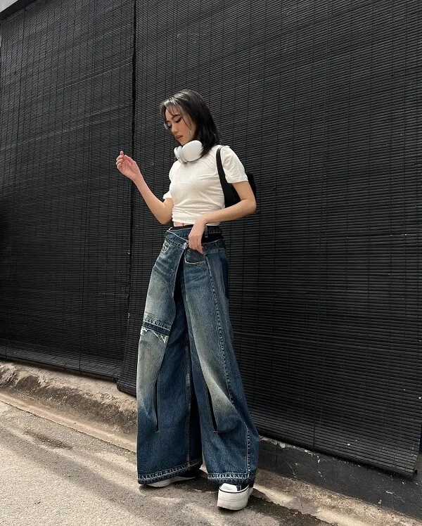 Bikini dieu nhi người phụ nữ đứng trước bức tường màu đen mặc áo phông trắng và quần jean xanh