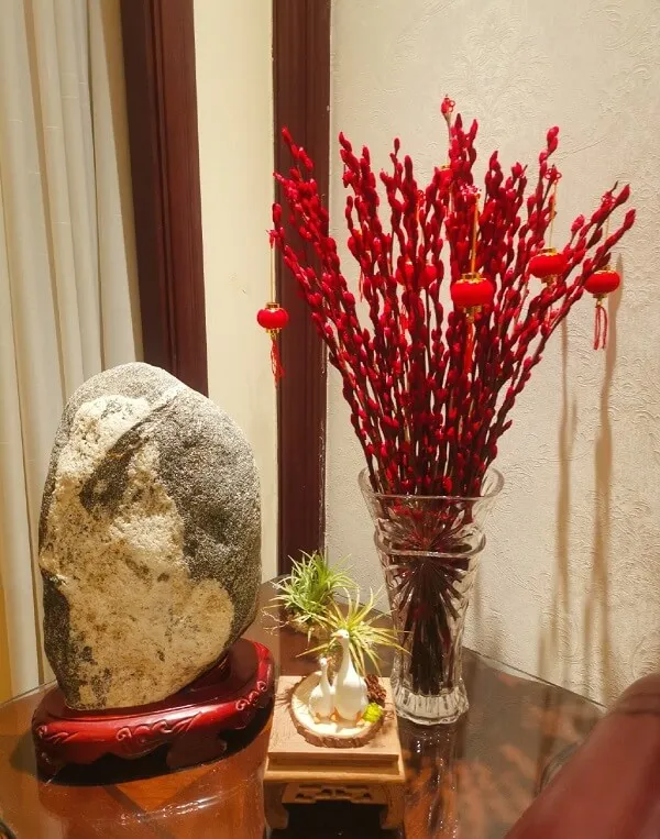 Cắm hoa tết có một chiếc bình với những bông màu đỏ và tảng đá trên bàn