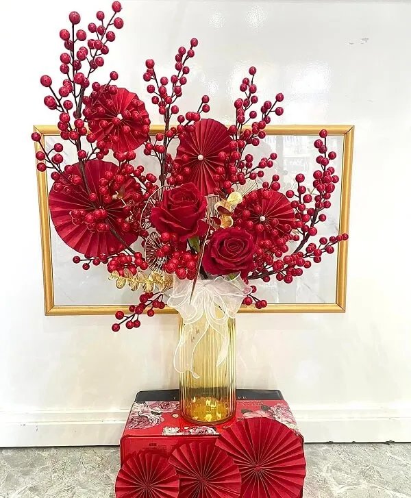 Cắm hoa tết có một chiếc bình với những bông màu đỏ trong đó ngồi trên bàn