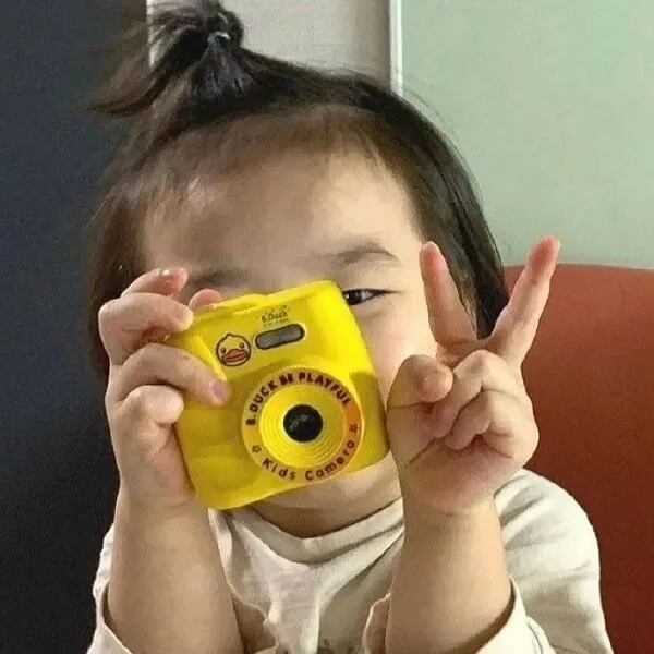 Có một cô bé cầm chiếc máy ảnh màu vàng lên mặt