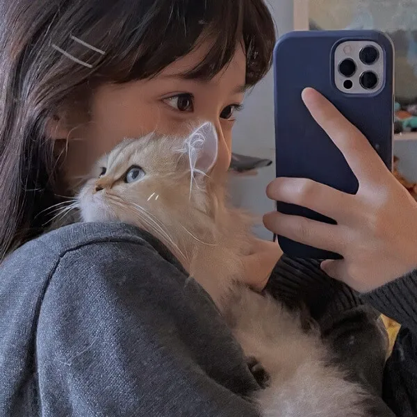 Có một người phụ nữ cầm con mèo và chụp ảnh với điện thoại của mình