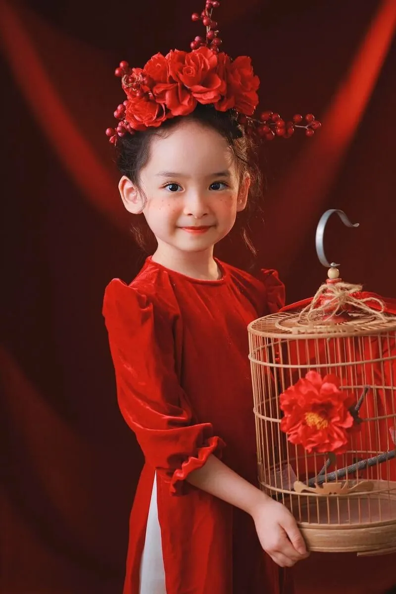 Concept chụp ảnh tết cho bé có một cô gái trẻ mặc váy đỏ cầm lồng chim