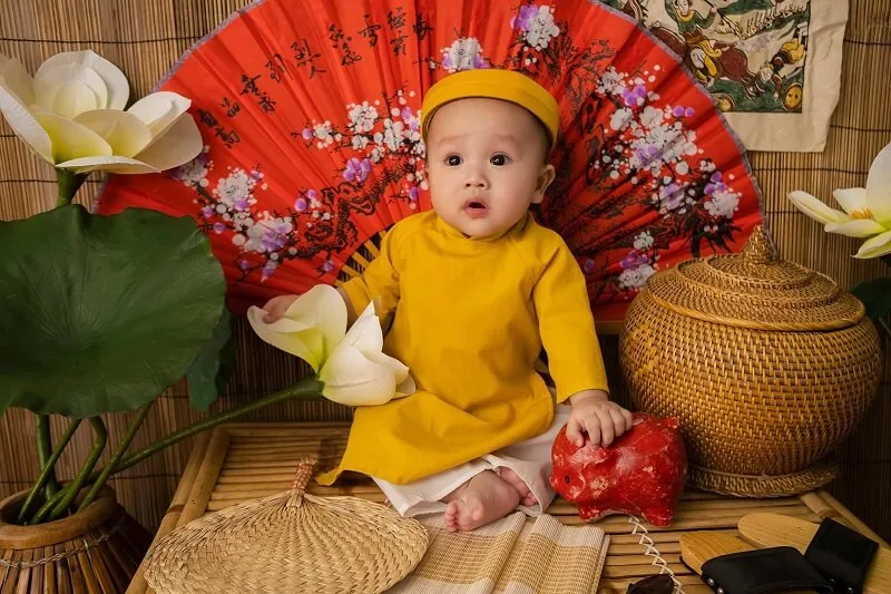 Concept chụp ảnh tết cho be có một em bé đang ngồi trên tấm thảm với chiếc màu đỏ