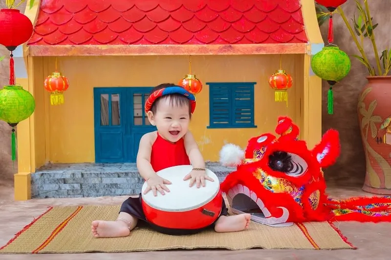 Concept chụp ảnh tết cho bé có một em đang ngồi trên mặt đất chơi với món đồ