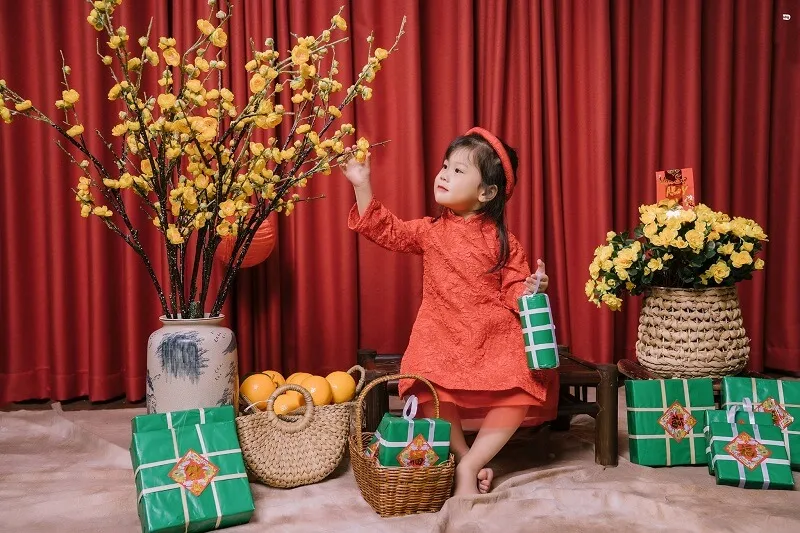 Concept chụp ảnh tết cho bé sơ sinh có một cô đang ngồi trên sàn với những món quà