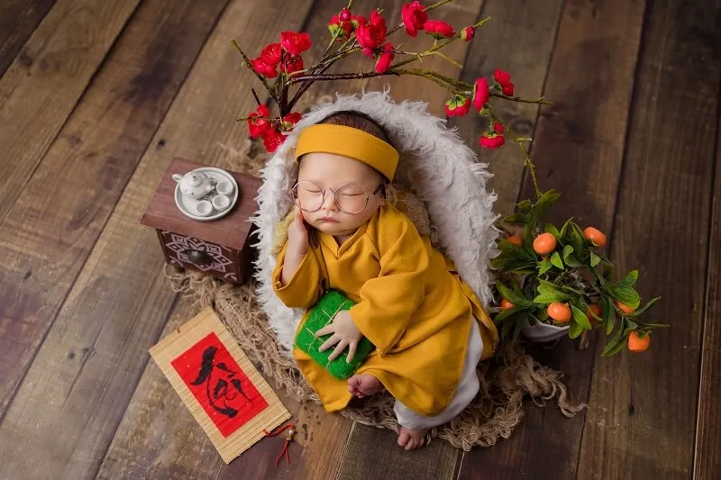 Concept chụp ảnh tết cho bé trai có một em ngủ trong cái giỏ với hoa trên sàn nhà