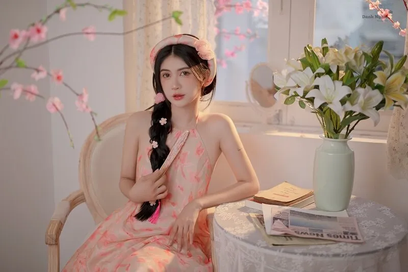 Phông chụp ảnh tết có một người phụ nữ ngồi trên ghế bên cạnh chiếc bình hoa
