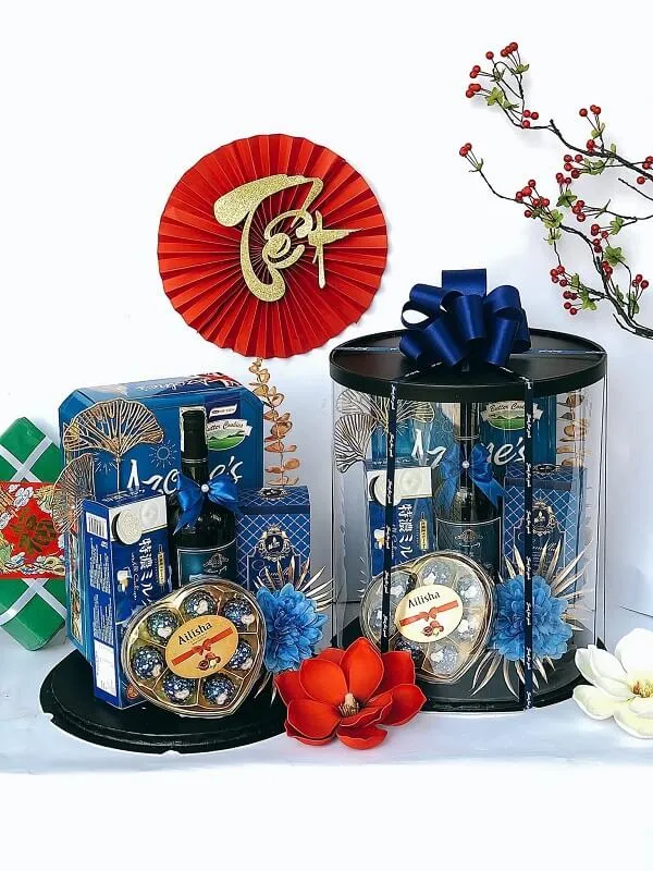 Giỏ quà tết chai rượu và đồng hồ trên bàn bên cạnh một chiếc bình có hoa hồng đỏ