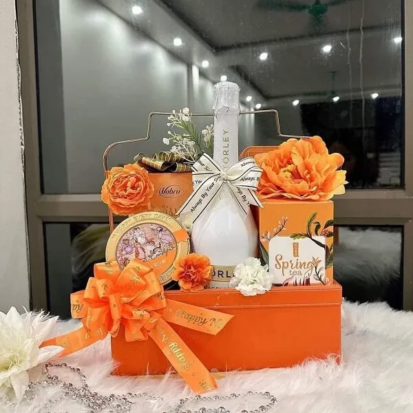 Giỏ quà tết có một hộp màu cam với chai rượu sâm banh và hoa