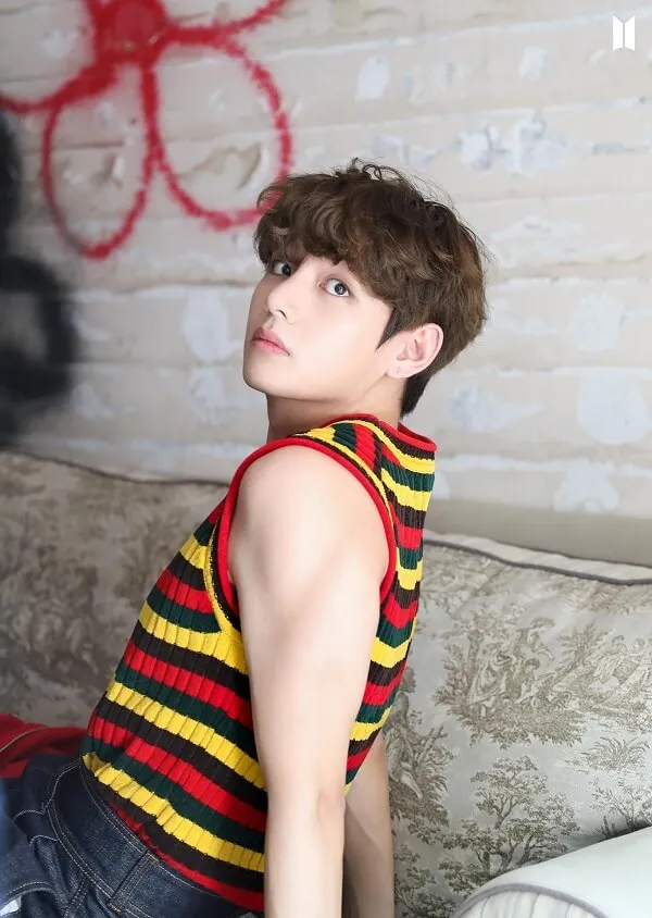 Hình ảnh bts có một chàng trai trẻ ngồi trên chiếc ghế dài mặc áo sơ mi sọc