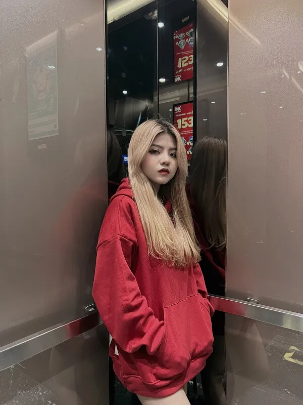Hình ảnh chị reency ngô có một người phụ nữ mặc áo hoodie màu đỏ đang đứng trong thang máy