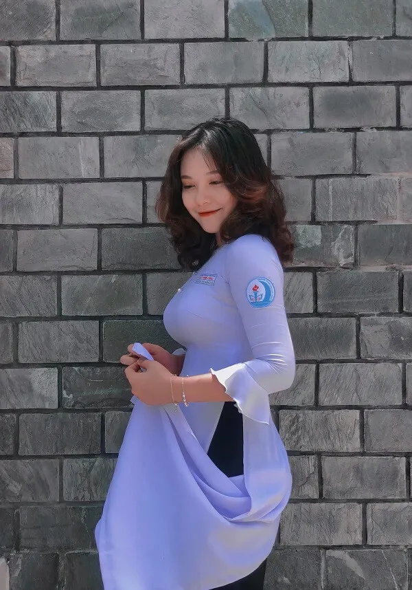 Hình ảnh gái xinh 2k5 người phụ nữ đang mặc một chiếc áo màu tím và quần đen đứng cạnh bức tường gạch