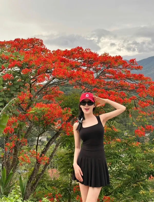 Người phụ nữ mang thai trong chiếc váy đen và mũ đỏ đứng trước cây với những bông hoa màu tươi