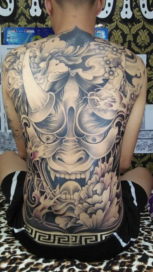Có một người đàn ông ngồi trên giường với hình xăm lưng