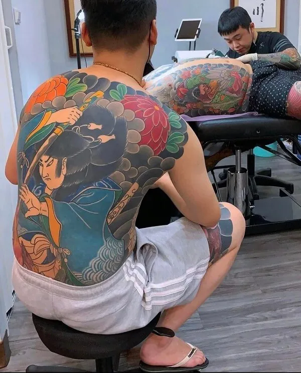 Có một người đàn ông ngồi trên ghế với hình xăm full lưng